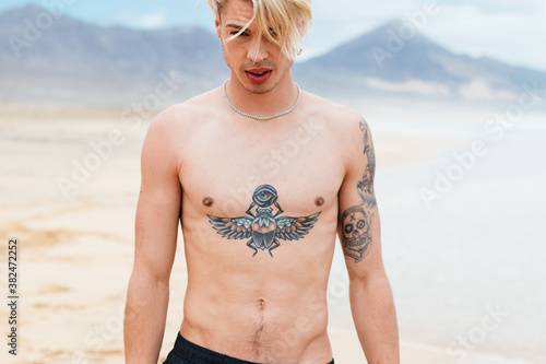 Tattooed handsome man walking along the beach photo