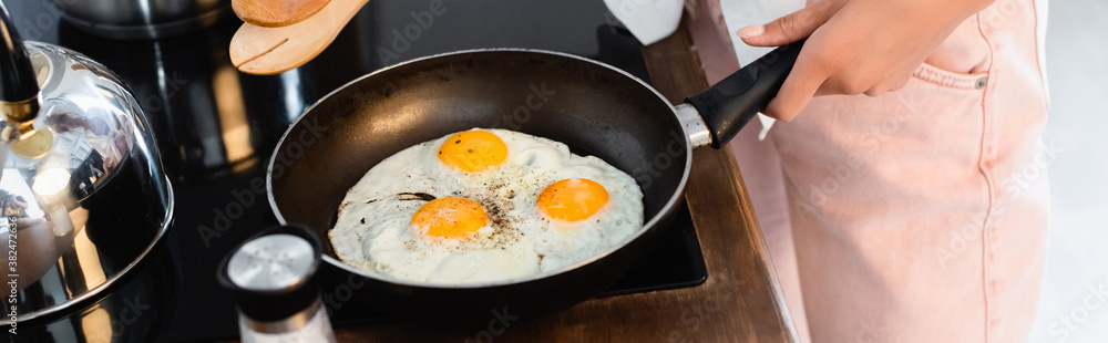 cropped view of woman holding kitchen tongs near eggs on frying pan, panoramic shot cropped view of woman holding kitchen tongs near eggs on frying pan, panoramic shot