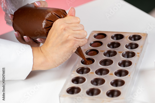 top view of chocolatier pouring caramel filling into chocolate mold preparing luxurious handmade Belgian candy. confectionary manufacturing small business idea concept. World Chocolate Day