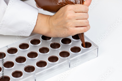 top view of chocolatier pouring caramel or praline filling into chocolate mold preparing luxurious handmade Belgian candy. confectionary manufacturing small business idea concept