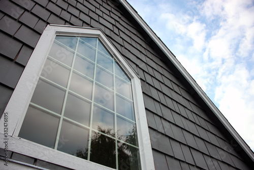 Large window with cloud reflections surrounded by white trim and gray shingles
