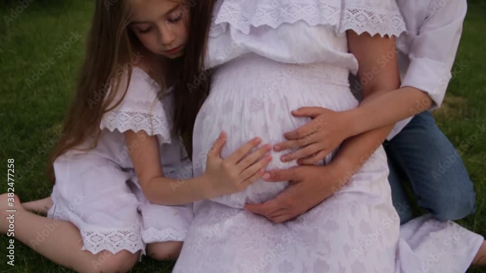 A pregnant mother with two children are walking in the garden near the house. Family with pregnant mom in the summer in nature. Children hugging pregnant belly A pregnant mother with two children are walking in the garden near the house. Family with pregnant mom in the summer in nature. Children hugging pregnant belly