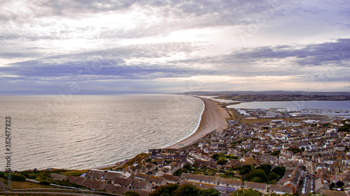 Beautiful hight view for cityscape on Isle of Portland in Unided Kingdom, photo showing a narrow shoreline leading to UK mainland, surrounding ocean with calm water and dramadic sky photo