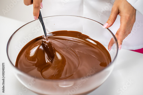 Closeup stirring mixing milk melted chocolate in glass bowl isolated on white background. Chocolatier make premium couverture hand-crafted chocolate. Candy making, pastry production, dessert concept photo