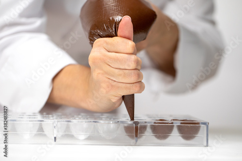 cropped view of chocolatier pouring melted dark chocolate into candy mold preparing luxurious handmade belgium confectionery. World Chocolate Day. Cooking video lessons. Culinary Blog concept
