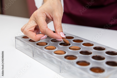 top view of confectioner adding almonds into caramel filling chocolate mold. chocolatier preparing luxurious handmade Belgian candy. preparation of premium handmade candies, truffles, chocolates