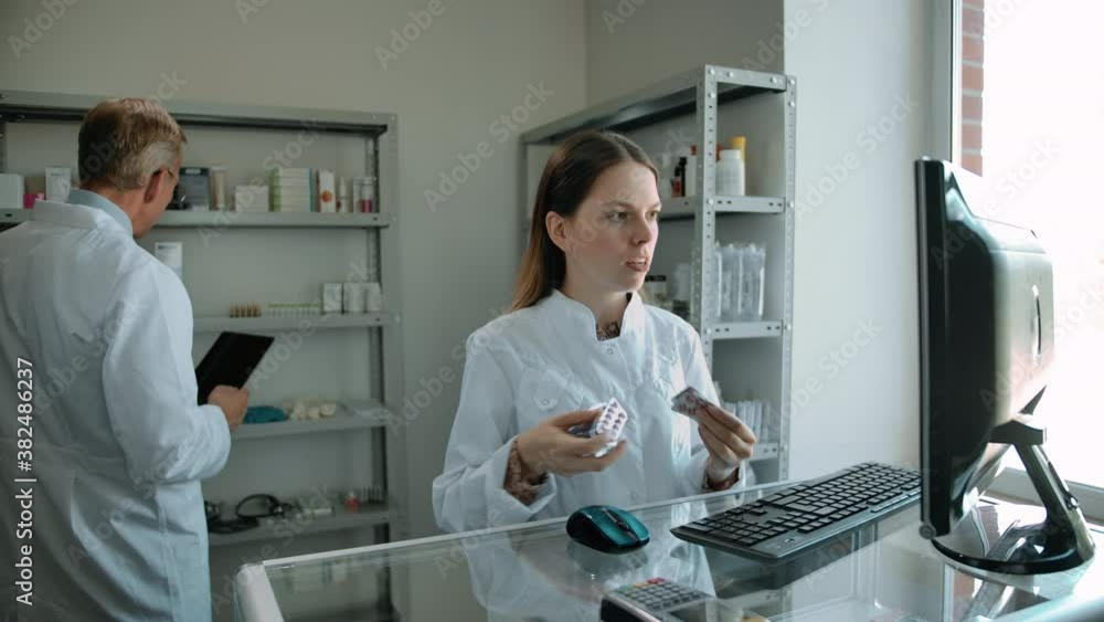 Young female asking her mature male colleague for medicines review. Two people in bright pharmacy interior communicating, preparing order for client. Young female asking her mature male colleague for medicines review. Two people in bright pharmacy interior communicating, preparing order for client.