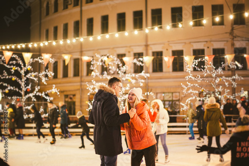 The theme is active recreation in winter on the ice arena. Young caucasian couple happy and in love glide together on an ice rink on christmas evening. Date at the skating rink on valentine's day