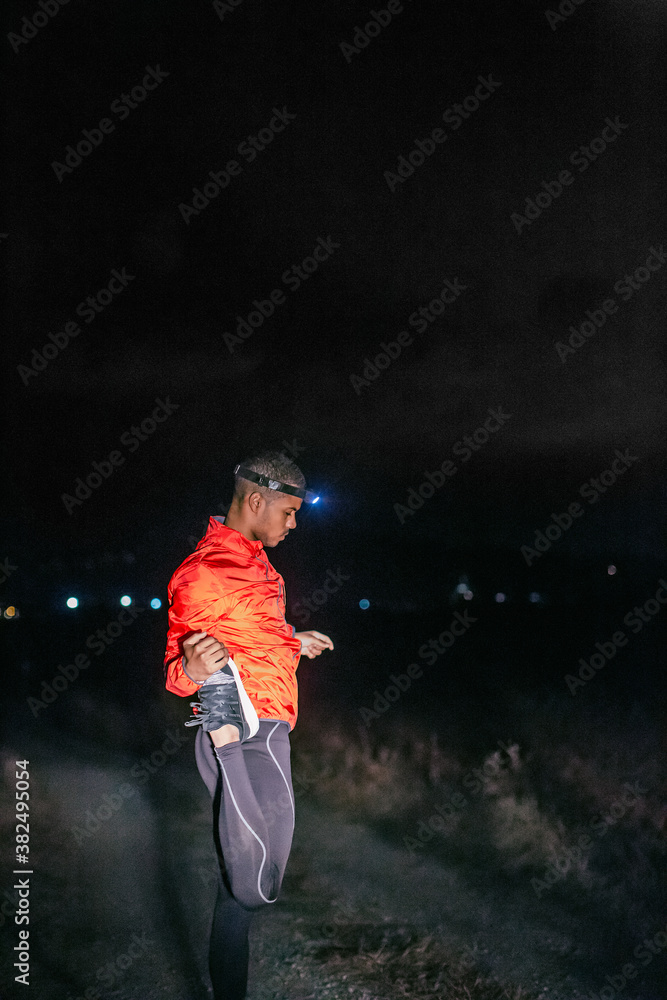 Side view of a runner doing stretching exercises on a field at night. Side view of a runner doing stretching exercises on a field at night.