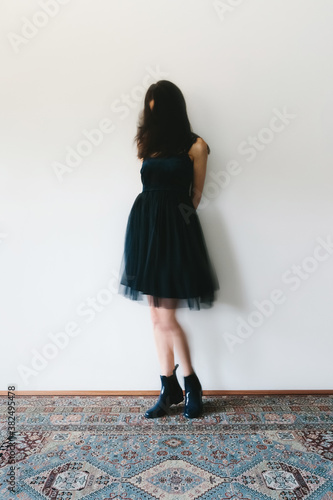 Movement shot of woman standing against a wall indoors, wearing party dress and plastic rain boots