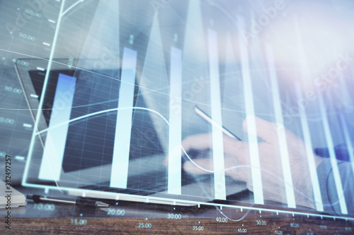 Double exposure of man's hands holding and using a digital device and forex graph drawing. Financial market concept.