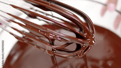 Close up sweet delicious dark melted chocolate on whisk that spins in slow motion. Making premium hand-crafted chocolate. Preparing pralines, candy or truffles concept, pastry, bakery, patisserie