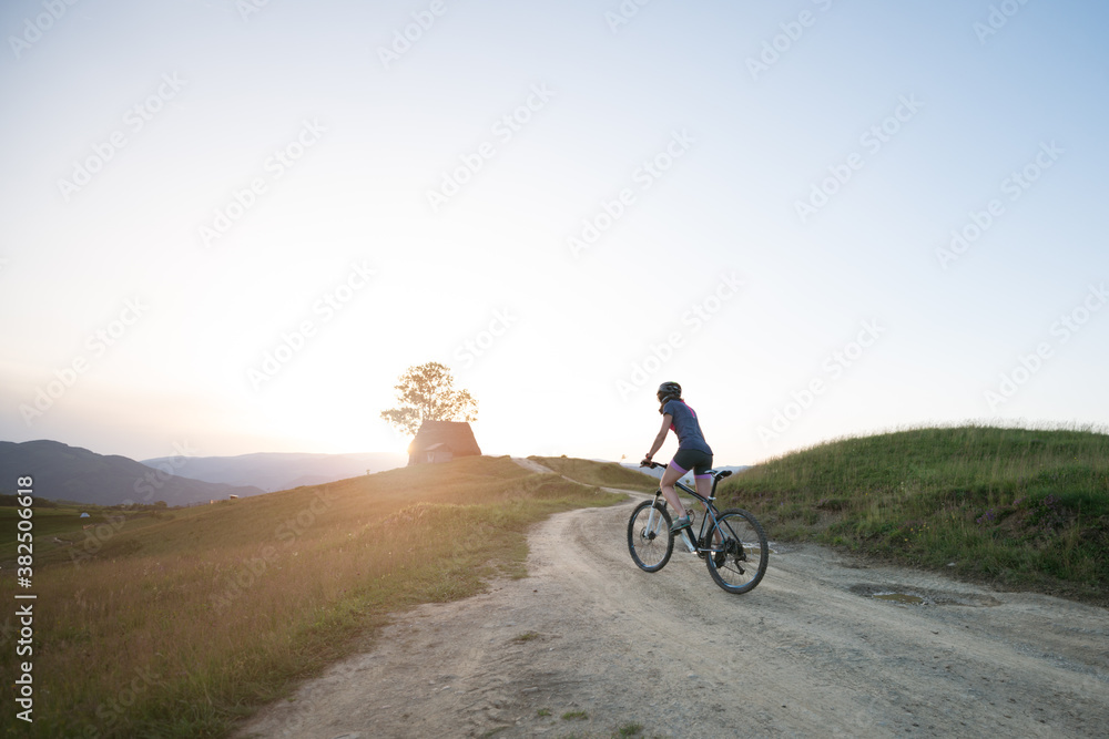 Female riding mountain bike along a mountain trail during susnet Female riding mountain bike along a mountain trail during susnet