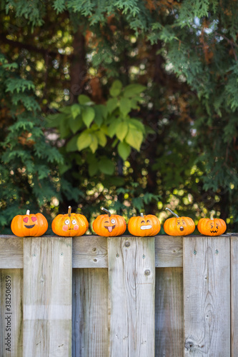 Pumpkins with emoticon faces lined up on a fence photo