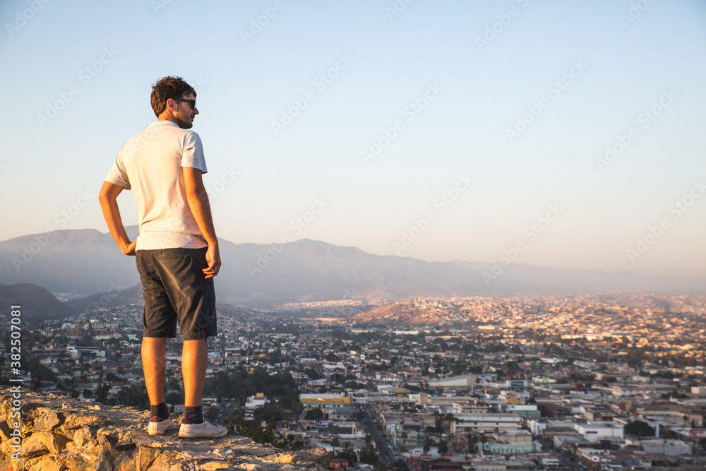 Young man standing on top of a wall overlooking a city at sunset from a viewpoint Young man standing on top of a wall overlooking a city at sunset from a viewpoint