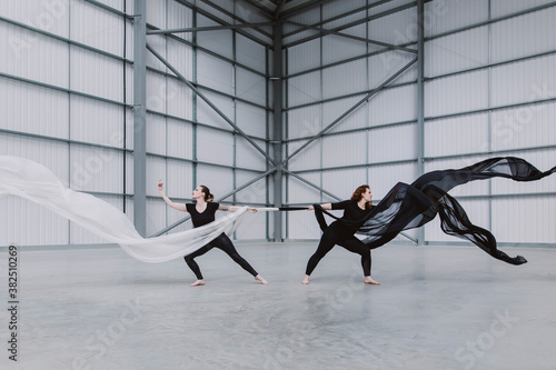Two female dancers holding onto black and white silk, leaning and balancing away from each other