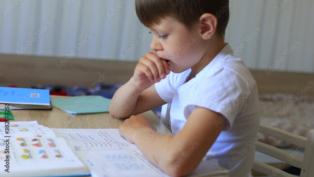 A child does homework on isolation. Homework. Distance learning. A boy writes a math lesson in a notebook. A child does homework on isolation. Homework. Distance learning. A boy writes a math lesson in a notebook.