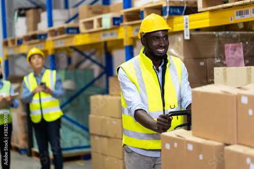 Black Male warehouse worker pulling a pallet truck. middle aged African American warehouse worker preparing a shipment in large warehouse distribution centre