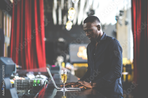 handsome young African American man looking at laptop computer screen. Black businessman working on laptop computer at the club.