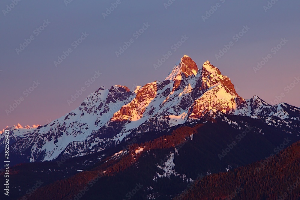 Canadian and American Border Peak Mountain covered in snow with last sun rays during red sunset in winter, British Columbia, Canada