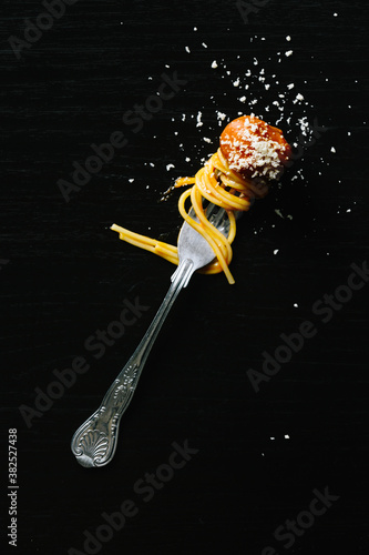 Fork with spaghetti and meatball on black with sprinkled parmesa photo