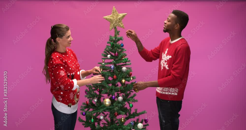 Studio shot of woman and man putting finishing touches on decorated christmas tree, slow motion Studio shot of woman and man putting finishing touches on decorated christmas tree, slow motion