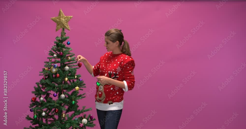 Studio shot of a smiling woman decorating a christmas tree, slow motion Studio shot of a smiling woman decorating a christmas tree, slow motion