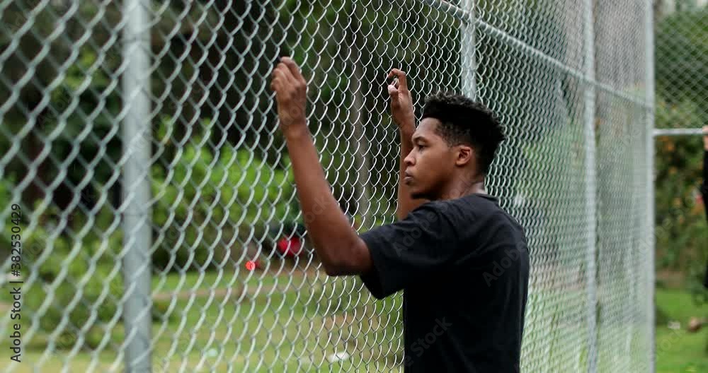 Pensive young black man leaning on metal fence. Contemplative mixed race person Pensive young black man leaning on metal fence. Contemplative mixed race person