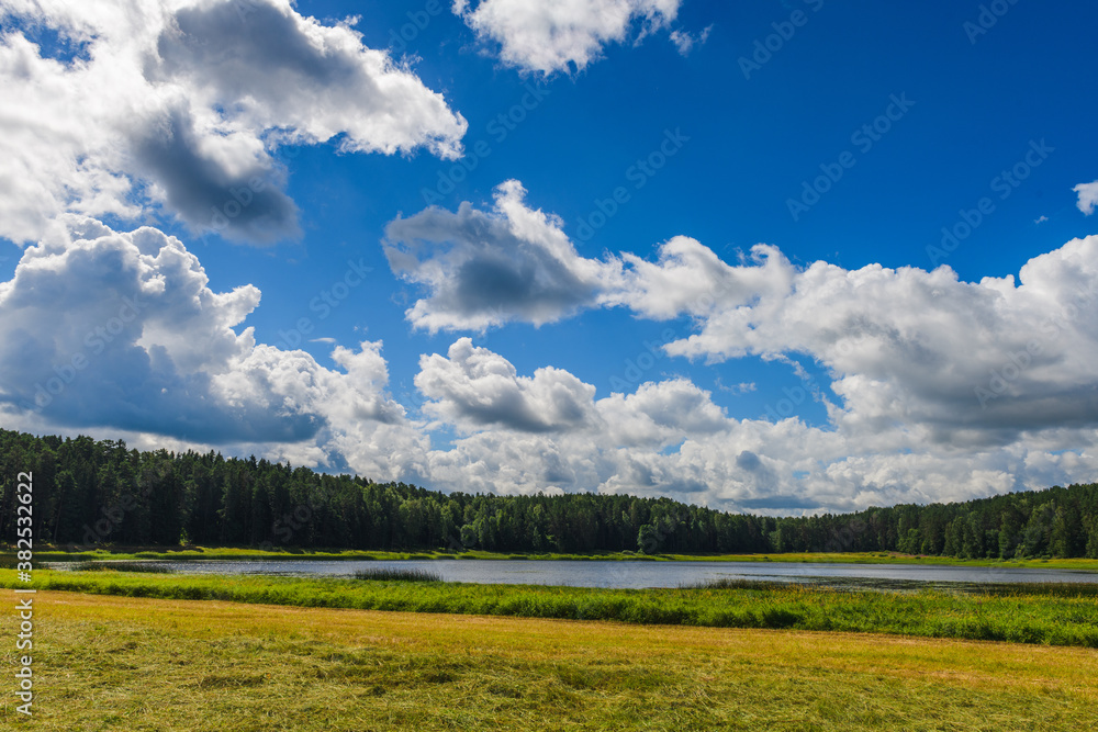 Stunning landscape with a lake, field, haystacks and gorgeous clouds in the sky