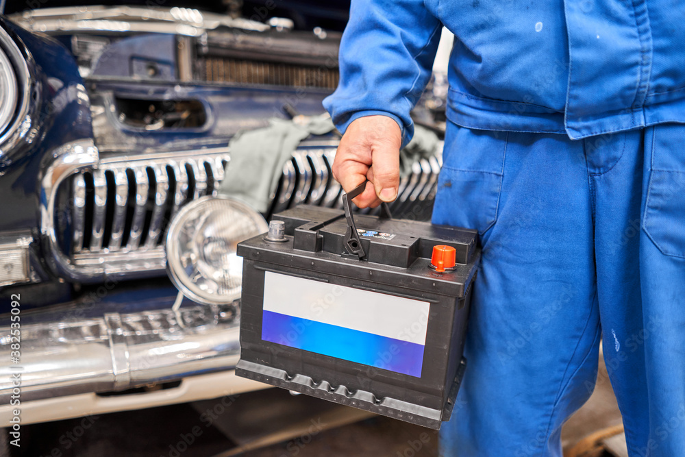 Engine engineer is replacing car battery because car battery is depleted. concept car maintenance. Against the background of a retro car of the 50s Engine engineer is replacing car battery because car battery is depleted. concept car maintenance. Against the background of a retro car of the 50s