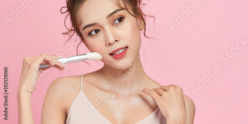 pretty girl take makeup brush in dress isolated on a pink background