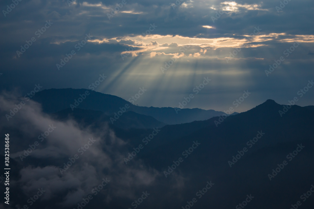beautiful landscape of hills silhouette during sunrise. light breaking through cloud cover.