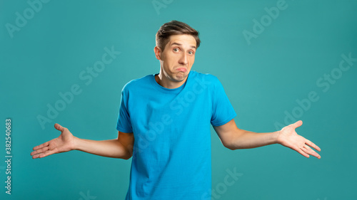 Puzzled male portrait. Careless gesture. Helpless emotion. So what. Doubtful expressive man shrugging looking at camera isolated on blue.