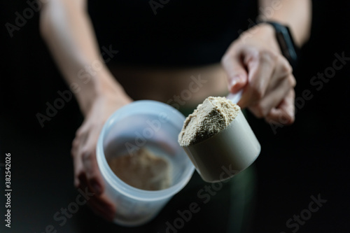 Close up of women with measuring scoop of whey protein and shaker bottle, preparing protein shake. photo