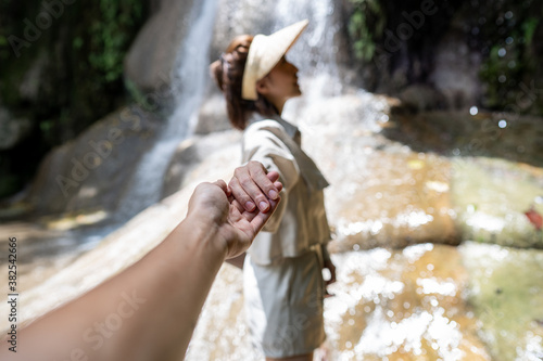 Fototapeta Naklejka Na Ścianę i Meble -  Woman holding her boyfriend hand .walk to waterfall in tropical rainforest. Saiyok noi Waterfall, Located in Kanchanaburi province, Thailand.