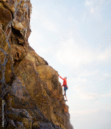 Senior male rock climber, climbing steep rock face, with seascape in the background. photo