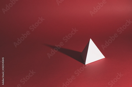 A white paper tetrahedron sits on a red background casting long shadow... photo