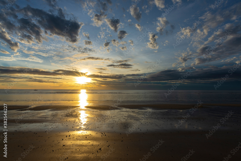 Beautiful sunrise above sea or ocean and small clouds on the sky, reflection of sun in the water and sand on beach