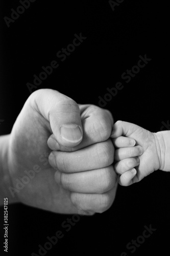 B&W photo,Fist of Dad and Newborn Baby,isolated on black background.