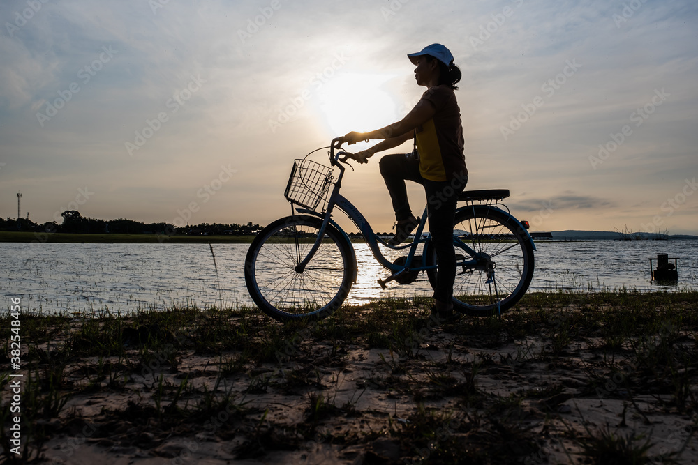 Fototapeta premium Silhouette of women with vintage bicycle near the beach during sunrise.
