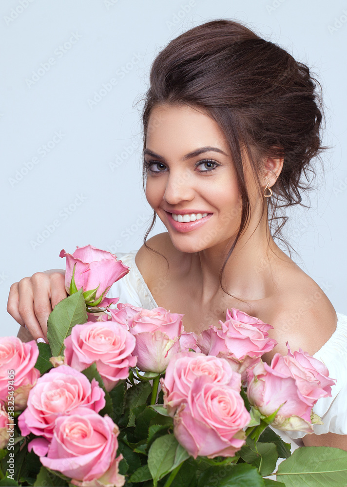 Beautiful young woman with a big bouquet of roses flowers in a white dress on a light background Beautiful young woman with a big bouquet of roses flowers in a white dress on a light background