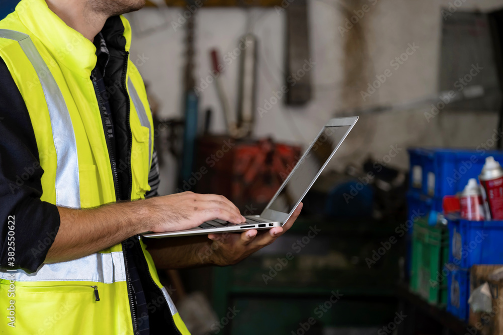 Confident of engineer or worker wearing a safety jacket and typing keyboard on the laptop which shown back screen. Working in manufacturing, Many tools, and spray bottles. Industrial concept