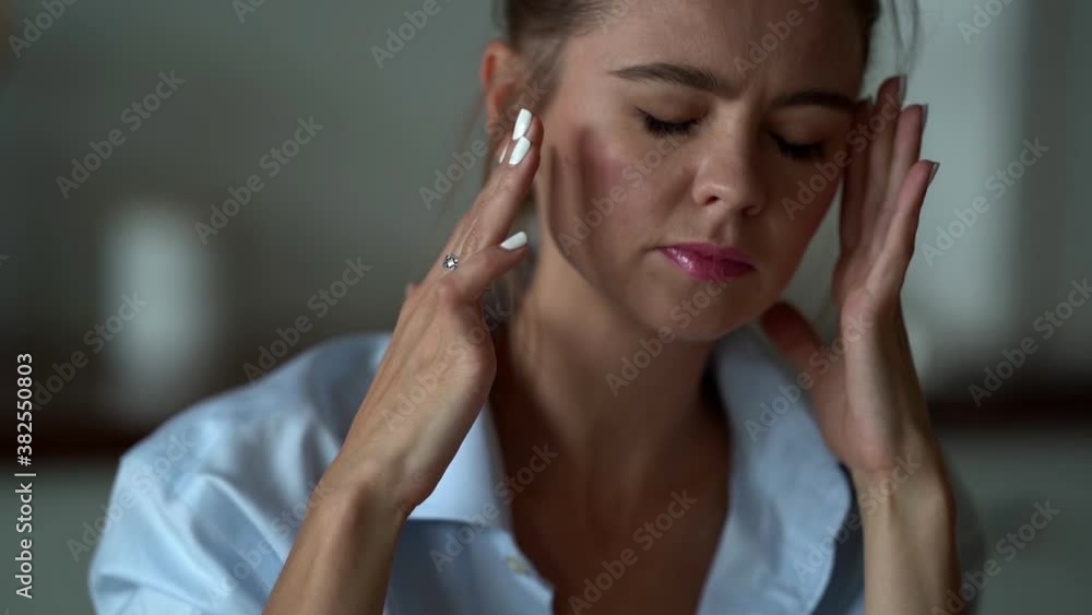 Close-up portrait of a sad woman in a shirt sitting at home, her head hurts, she touches her head with her hands and massages her temples. Close-up portrait of a sad woman in a shirt sitting at home, her head hurts, she touches her head with her hands and massages her temples.