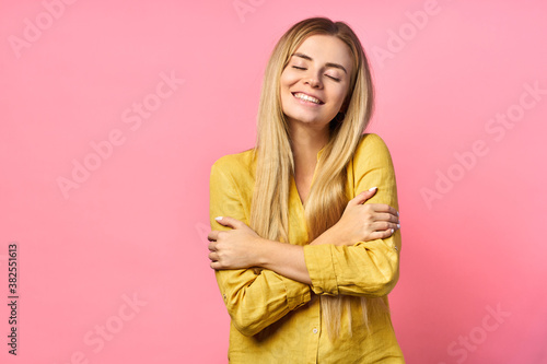 Sensual romantic woman, shows heart or love gesture, smiles happily, expresses affection, isolated on pink wall. blonde hugs herself.