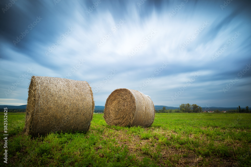 Hayrolls on a field with dramatic clouds long exposure