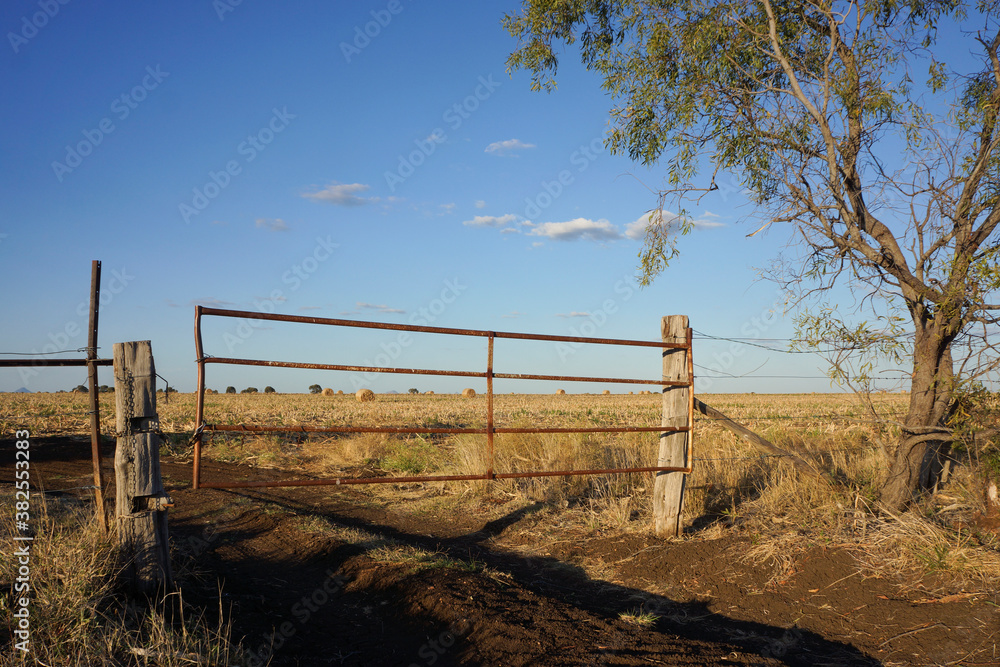 Rustic farm gate with track leading to hay bales.