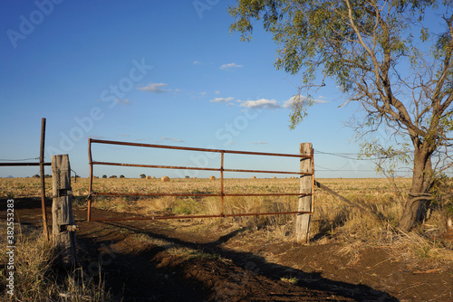 Rustic farm gate with track leading to hay bales.