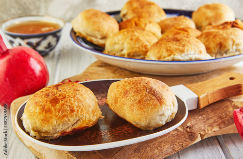 Asian baked meat pies - samsa or sambousak in a national plate with pomegranate, Middle Eastern cuisine on a wooden white table