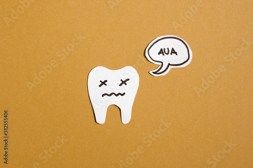 Ein Zahn auf gelbem Hintergrund, der Schmerzen hat und eine Sprechblase in der Aua steht. Zahnarzt. Zahnschmerzen. Karies.