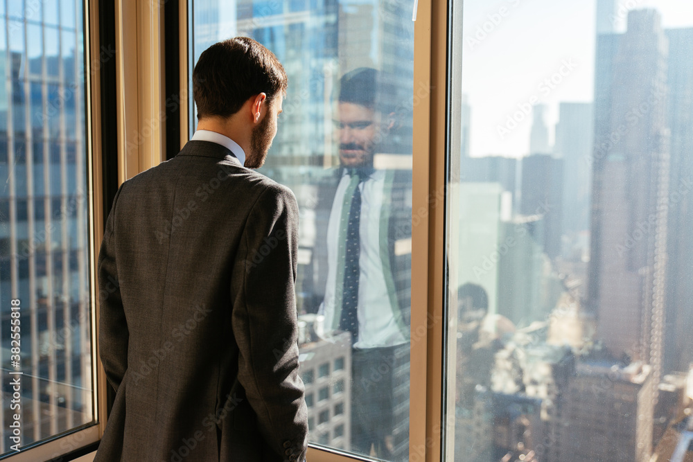 Businessman looking through window at city from the office Businessman looking through window at city from the office